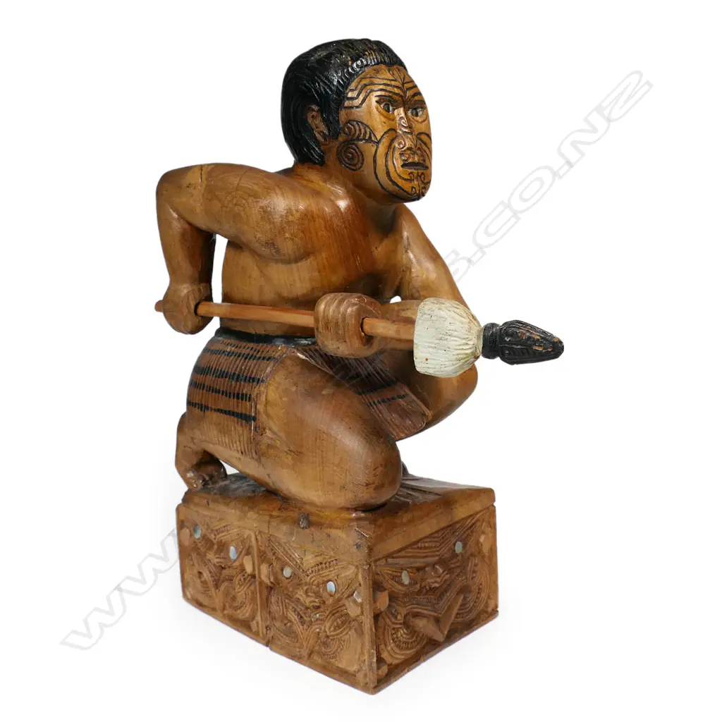 A carved folk art Māori warrior, kneeling with taiaha, carved on block with wheku carved to each side. H.310mm. Image 1++