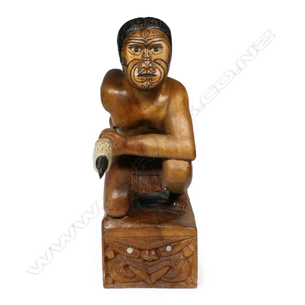 A carved folk art Māori warrior, kneeling with taiaha, carved on block with wheku carved to each side. H.310mm. Image 1++