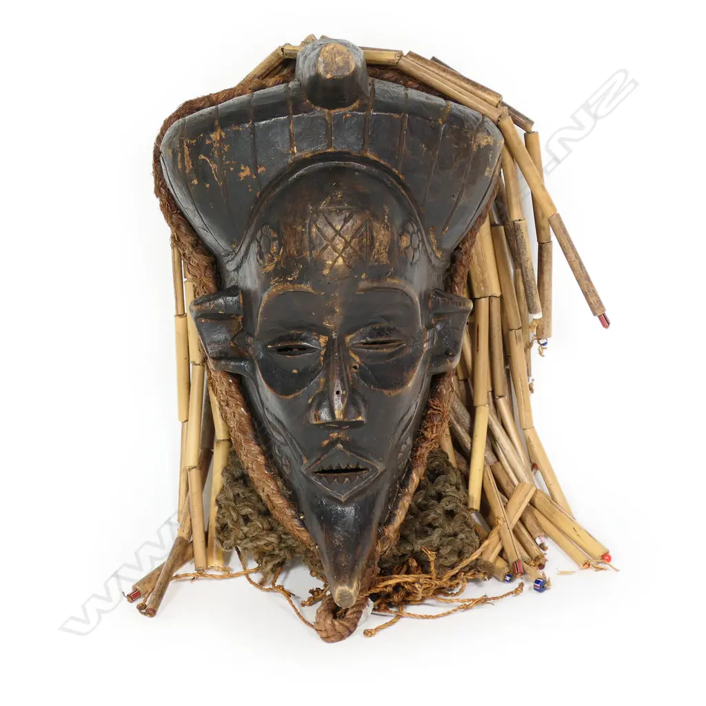 African mask probably Chokwe Mwana Pwo. Carved wood with woven fibre border with bamboo sectional fringe. H.320mm. Provenance: Ex. The Estate of John Perry. Image 1++