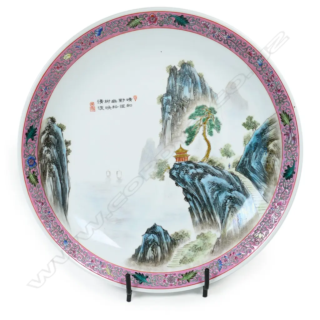 A large Chinese porcelain charger painted with a mountainous landscape scene within a pink famille rose border' The centre with short inscription. Made in China mark to base indicating post 1958. Dia.330mm. Image 1++
