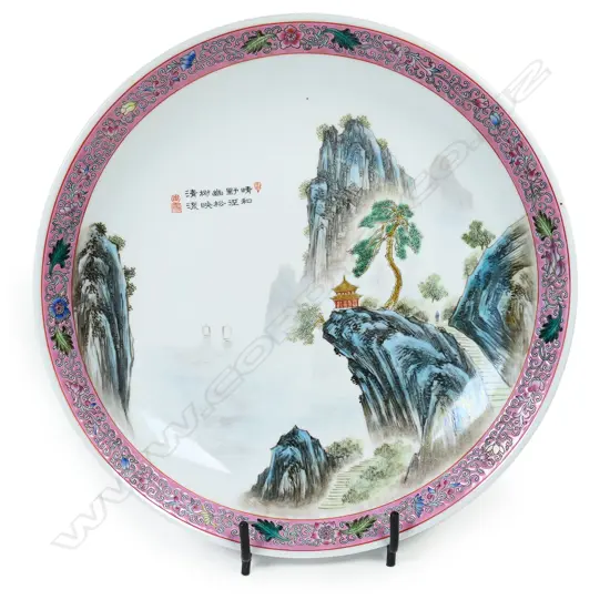 A large Chinese porcelain charger painted with a mountainous landscape scene within a pink famille rose border' The centre with short inscription. Made in China mark to base indicating post 1958. Dia.330mm.