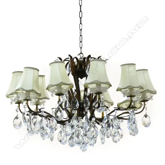 A mid 20thC French style ormolu chandelier, the 10 scrolling arms with acanthus leaf highlights, cut glass drip trays and multiple facetted pendant drops. Each light with a cream silk shade. Dia.800mm.