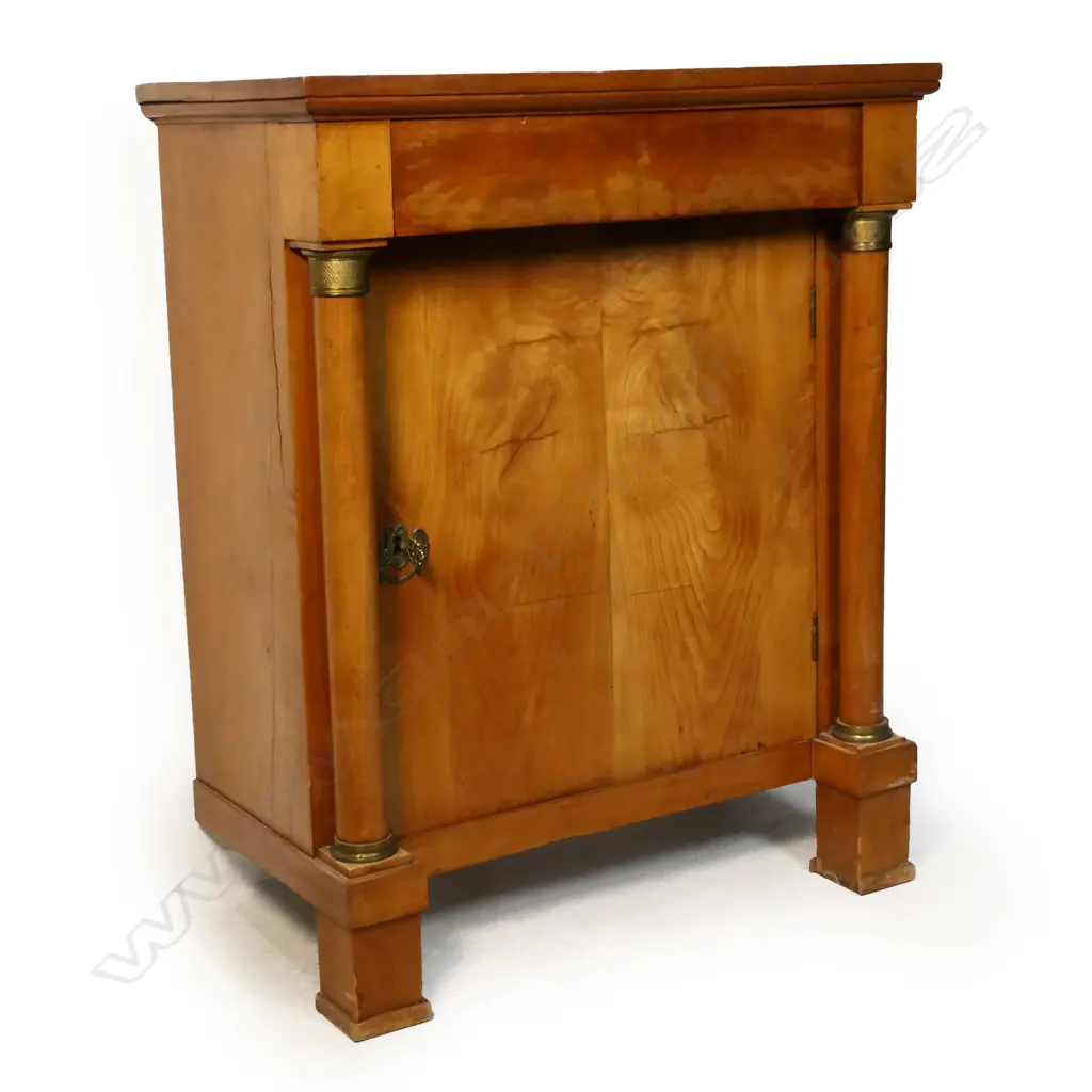 A birch Biedermeier cabinet: frieze drawer over one door and column to each side with brass detail. Raised on square section feet -  one absent. 730 x 390 x 910mm. Image 1++