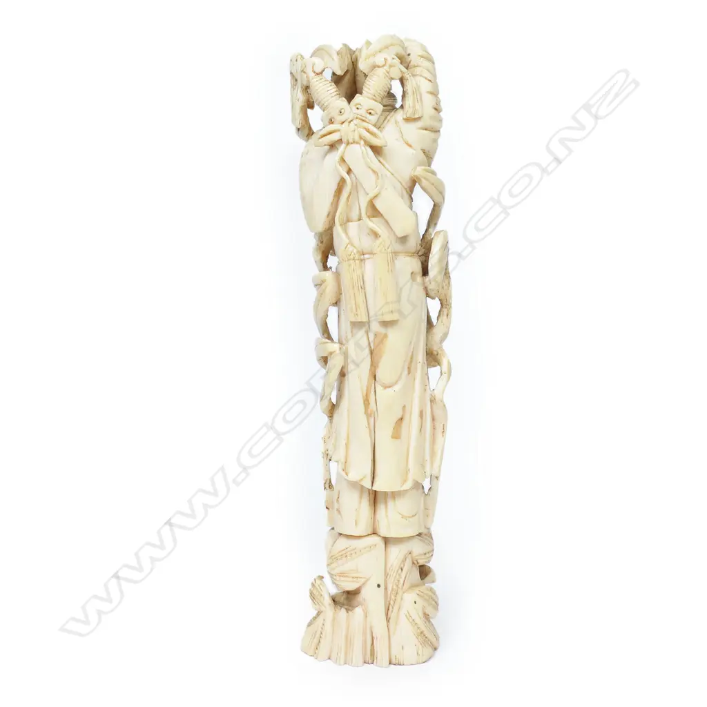 A Japanese ivory figure of a temple guardian, standing bearing crossed swords behind his shoulders, his limbs and body flanked by ribbon scrolls. On pegged base. H.175mm Image 1++
