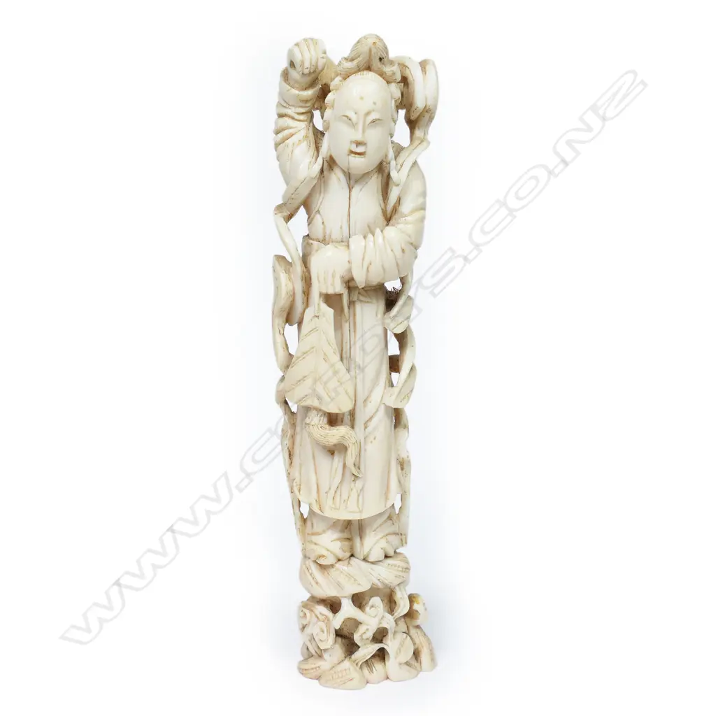 A Japanese ivory figure of a temple guardian, standing bearing crossed swords behind his shoulders, his limbs and body flanked by ribbon scrolls. On pegged base. H.175mm Image 1++