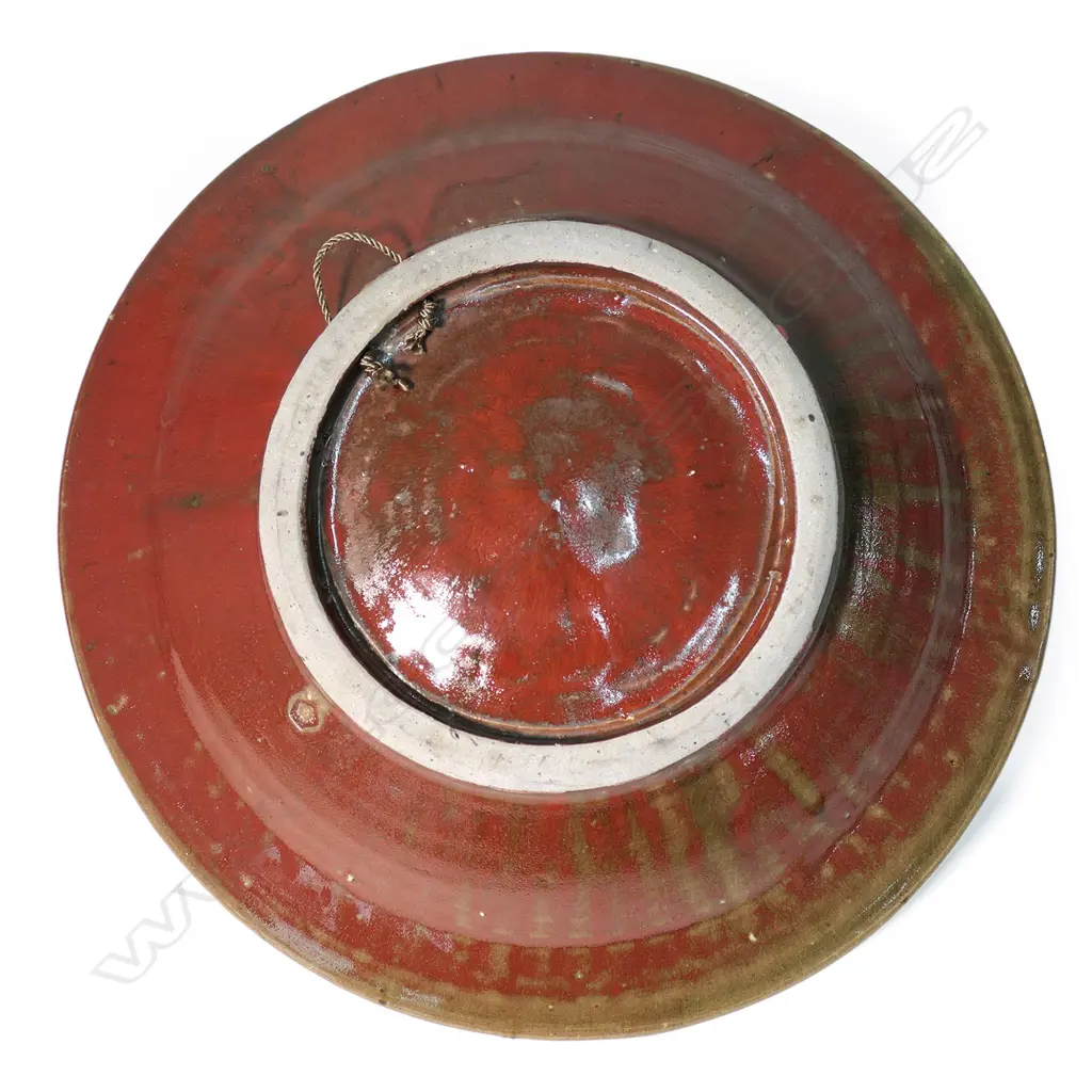 Mirek Smisek red glazed wall charger; the rim with impressed with diamond and triangular repeating motif. Impressed potter's mark to reverse and with rope suspension. Dia.400mm. Image 1++