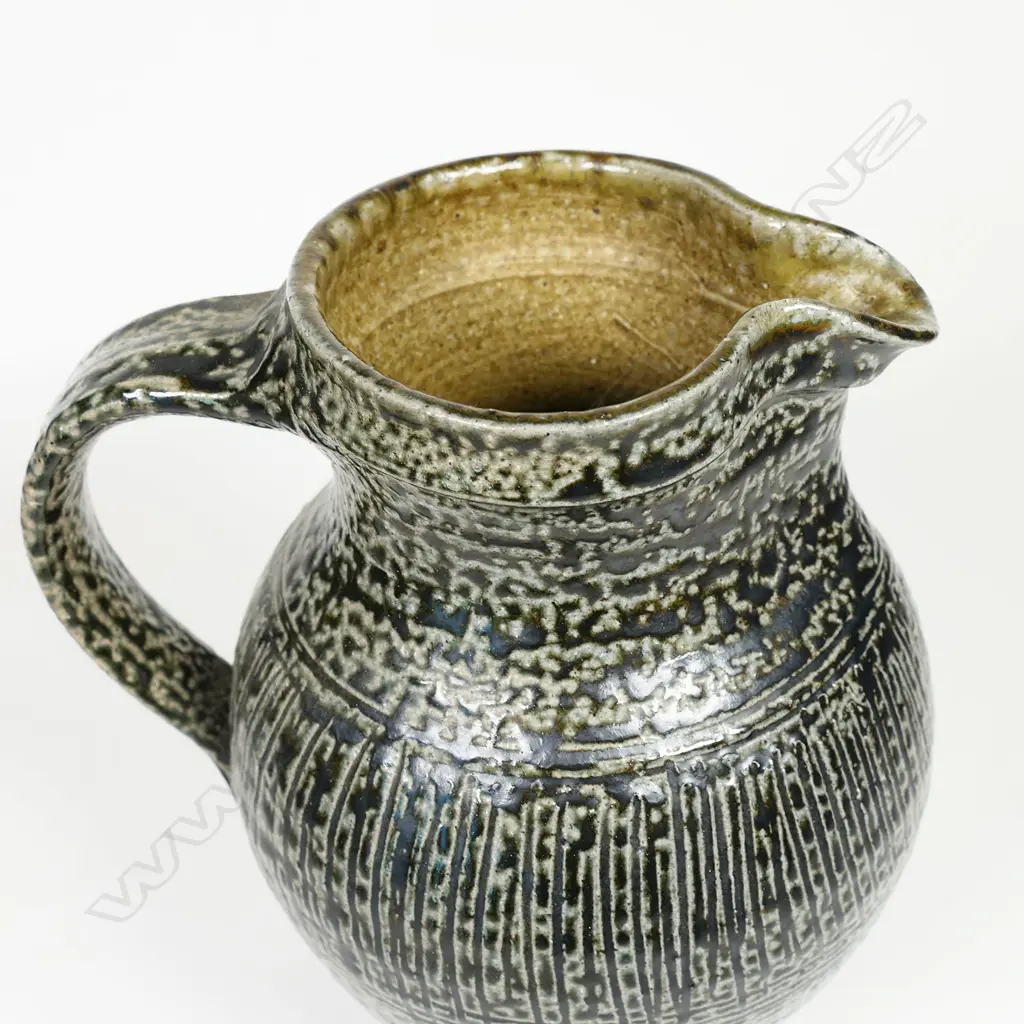 Mirek Smisek early salt glazed jug with a mottled grey/brown glaze and band of finely incised pattern to middle. Impressed potter's mark. H.170mm Image 1++