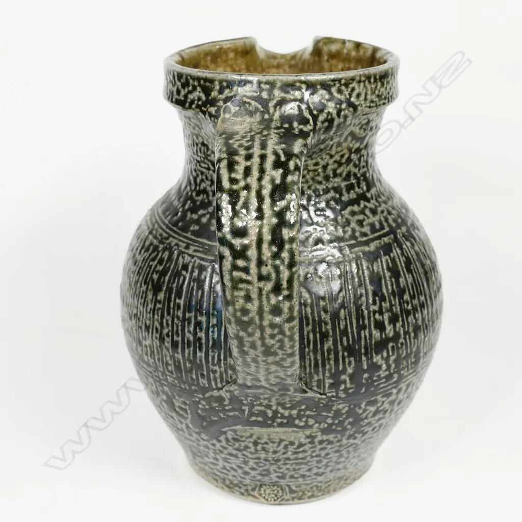 Mirek Smisek early salt glazed jug with a mottled grey/brown glaze and band of finely incised pattern to middle. Impressed potter's mark. H.170mm Image 1++