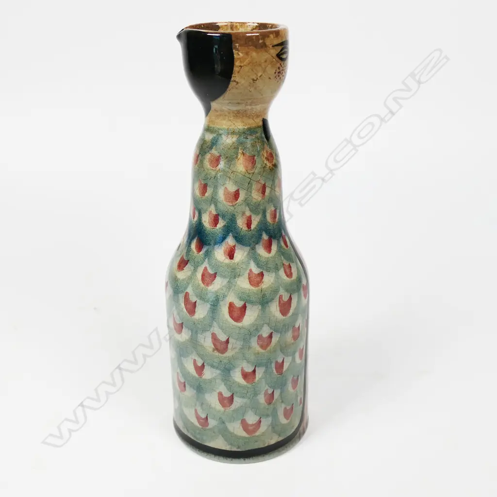 Frank Carpay for Crown Lynn figural oil bottle. The cylinder body decorated with restrained repeated fabric motif and stylised facial detail - pouring lip to rear. HANDWERK H.9-7 signature and Crown Lynn Tiki stamp to base. H.170mm. Image 1++