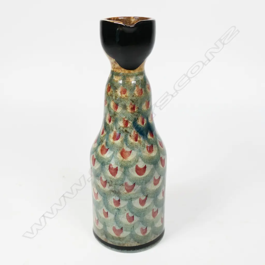 Frank Carpay for Crown Lynn figural oil bottle. The cylinder body decorated with restrained repeated fabric motif and stylised facial detail - pouring lip to rear. HANDWERK H.9-7 signature and Crown Lynn Tiki stamp to base. H.170mm. Image 1++