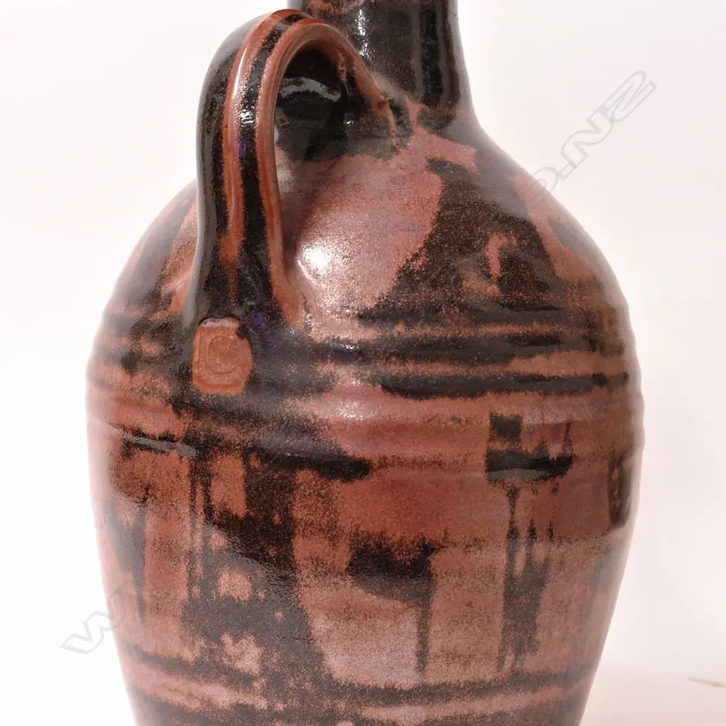 Crewenna Pottery (1962-1972 Harry & May Davis) flagon with dark tenmoku glaze - stylised decoration in lustrous dark red/brown tones, turned wooden topped cork stopper and tap. Potter's mark to base of strap handle. H.320mm. Image 1++