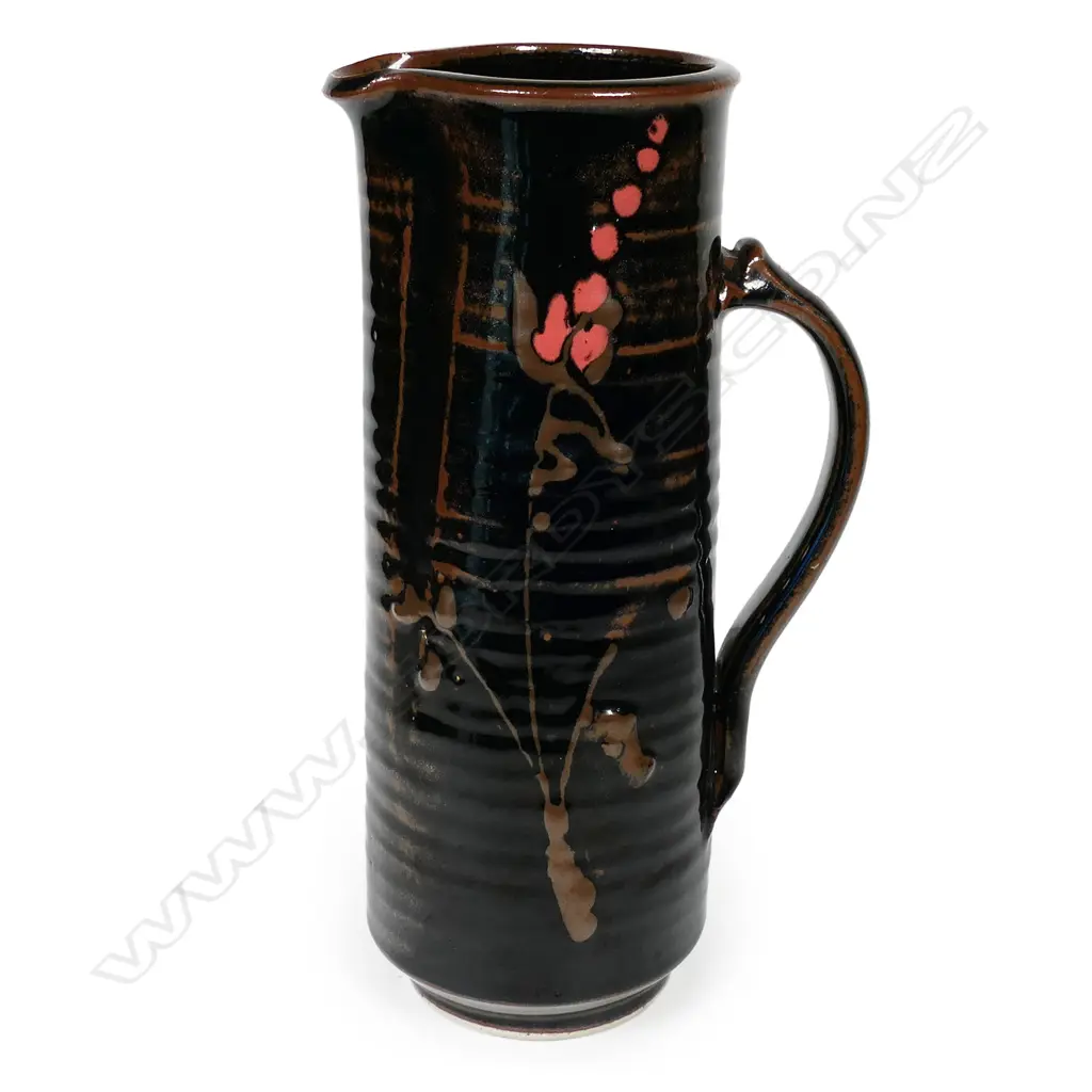 Peter Holmes tall cylinder jug with blossom decoration in brown and pink over lustrous tenmoku glaze. The jug reflects potter's interest in Japanese ceramics. Stamped mark at handle base. H.270mm Image 1++