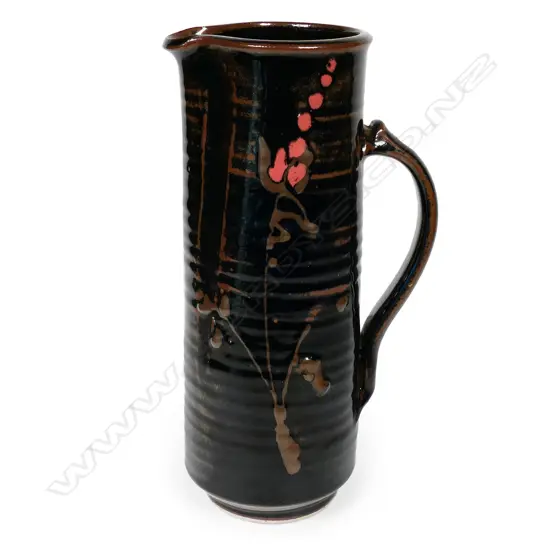 Peter Holmes tall cylinder jug with blossom decoration in brown and pink over lustrous tenmoku glaze. The jug reflects potter's interest in Japanese ceramics. Stamped mark at handle base. H.270mm