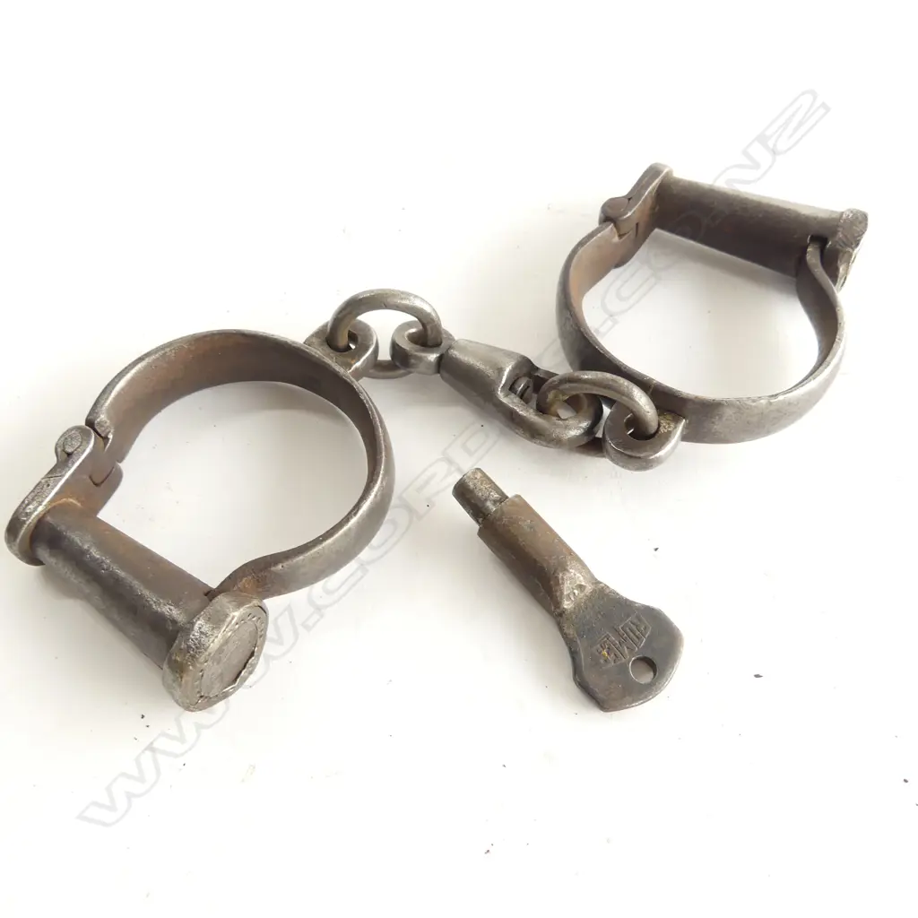 A pair of steel handcuffs with key, ‘Darby’ type, not adjustable, with swivel links between the manacles, the key marked Romer, various numbers to the cuffs. Image 1++