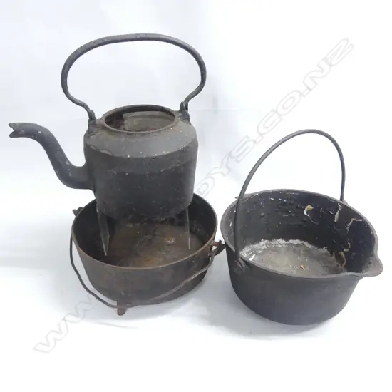 Two cast iron camp ovens and a kettle, lacking lids, one raised on three legs,