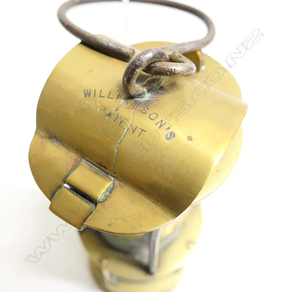 A Williamson's patent brass miner’s Safety Lamp, c.1900. Tapered cylindrical form with iron hook to the domed vented top, gauze section above the glass-covered lamp. Damage to internal glass. H.230mm Image 1++