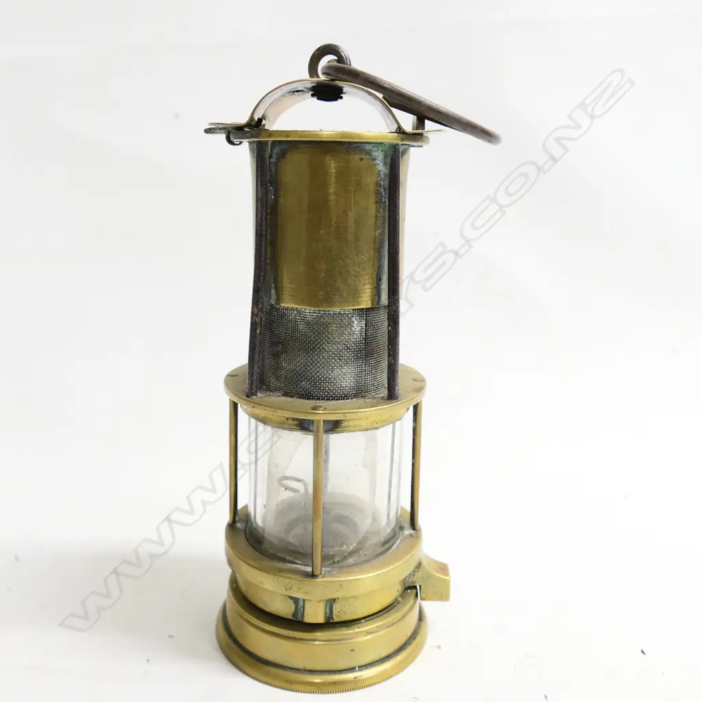 A Williamson's patent brass miner’s Safety Lamp, c.1900. Tapered cylindrical form with iron hook to the domed vented top, gauze section above the glass-covered lamp. Damage to internal glass. H.230mm Image 1++