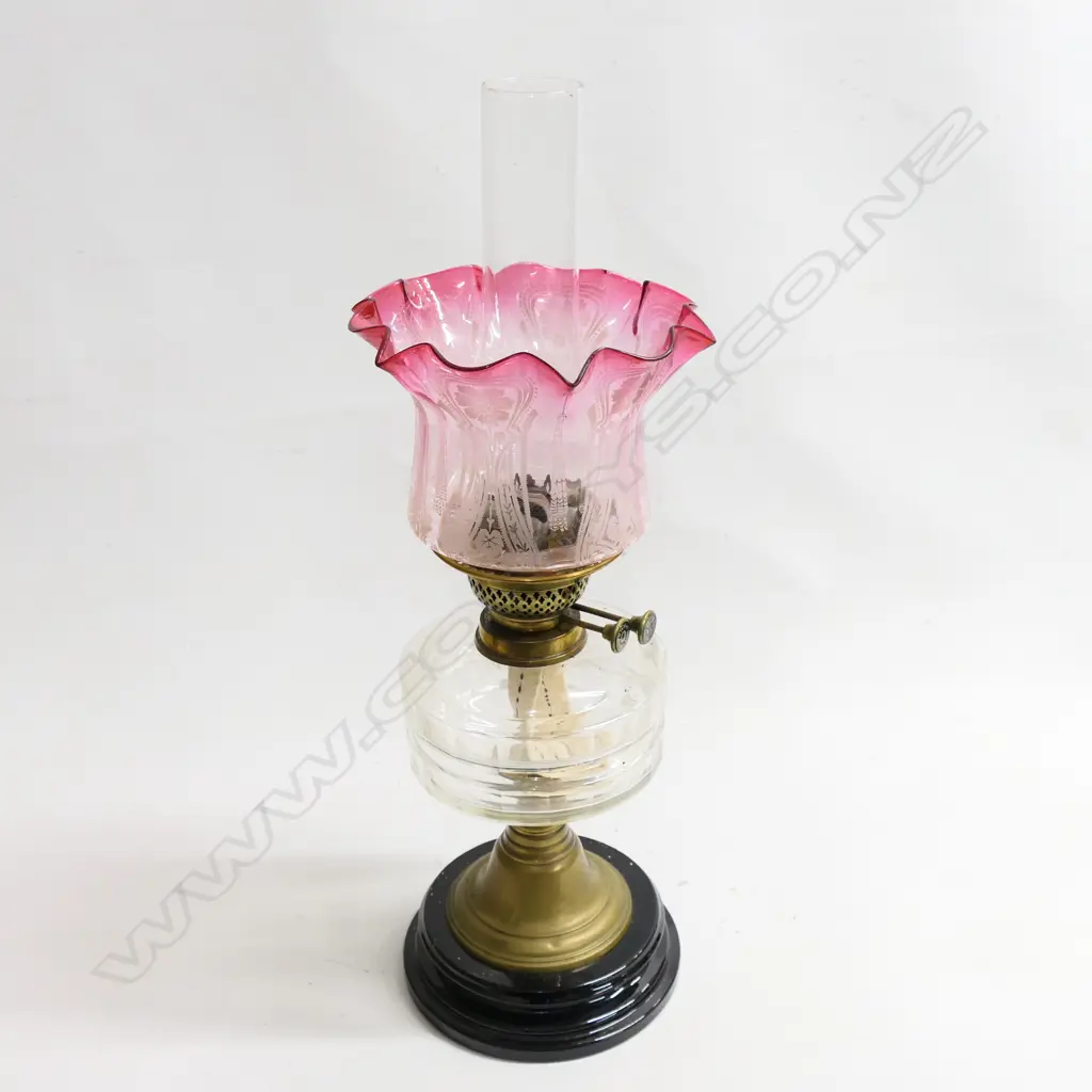A Victorian kerosene lamp with etched cranberry glass shade. The black china base and brass stand supporting a plain glass oil reservoir with two bands of cut decoration, H.540mmm Image 1++