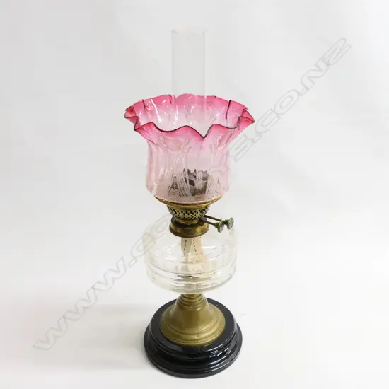 A Victorian kerosene lamp with etched cranberry glass shade. The black china base and brass stand supporting a plain glass oil reservoir with two bands of cut decoration, H.540mmm