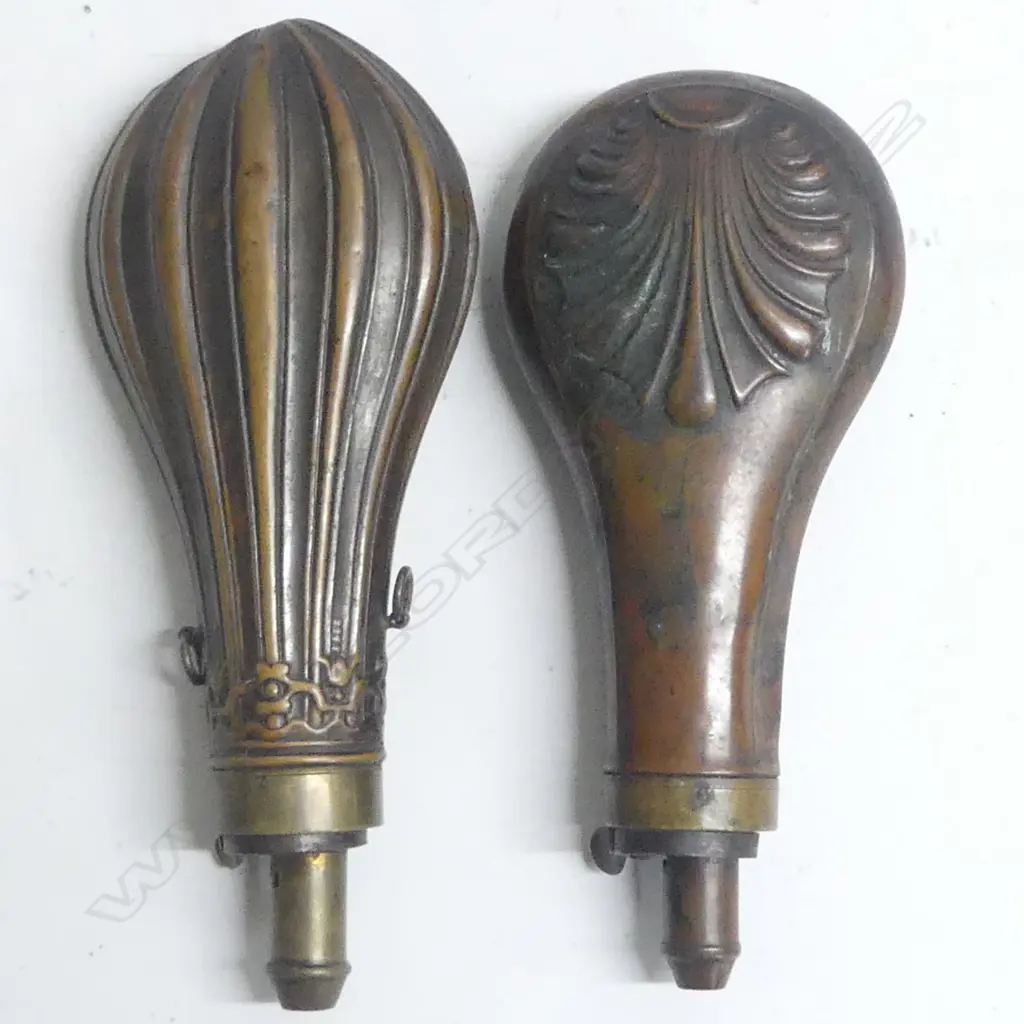 Two Victorian copper and brass powder flasks of bag shape with graduated dispenser nozzles one decorated with flutings beneath a foliate frieze at the shoulder, the other with a moulded anthemion design. Image 1++