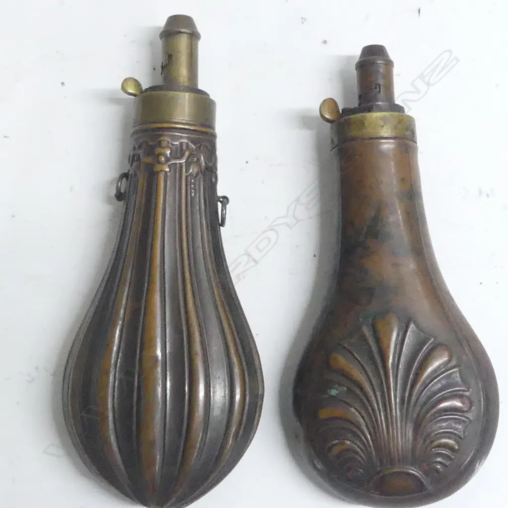Two Victorian copper and brass powder flasks of bag shape with graduated dispenser nozzles one decorated with flutings beneath a foliate frieze at the shoulder, the other with a moulded anthemion design. Image 1++