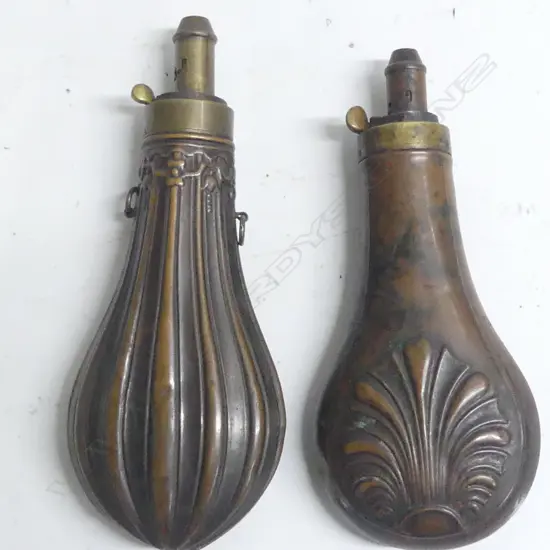 Two Victorian copper and brass powder flasks of bag shape with graduated dispenser nozzles one decorated with flutings beneath a foliate frieze at the shoulder, the other with a moulded anthemion design.