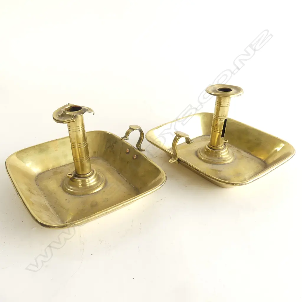 A pair of Victorian brass chambersticks, with wide rectangular drip-tray bases with flared rims, scroll handles, some damage and snuffers absent. . Image 1++