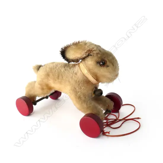 1314. With light tan wool plush; brown and black plastic eyes; red painted wooden wheels; button and tag in ear and paper label to bell.