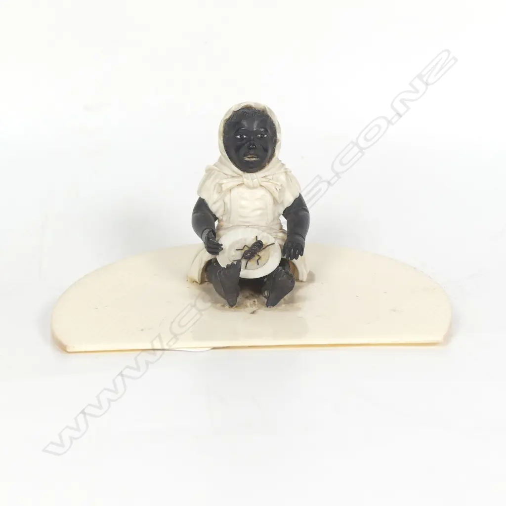 A racially caricaturing carved ivory and ebony figure of a black girl seated with a dinner plate carrying a single large cricket insect Image 1++