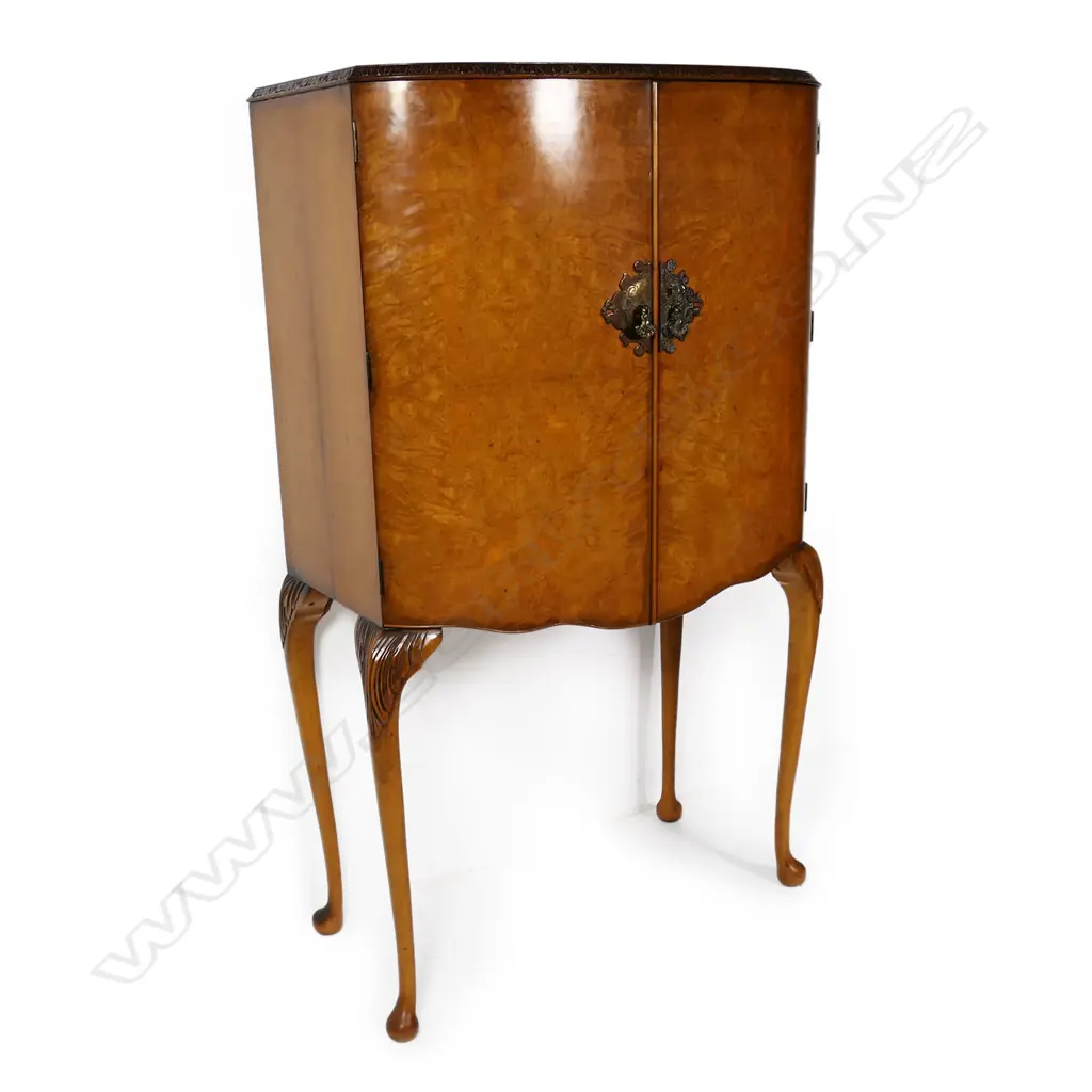 A c.1950 quality figured pale walnut drinks cabinet with the two bow front doors enclosing a mirrored back and base and with two glass shelves. Raised on cabriole legs with acanthus carved knees. 860 x 490 x 1480mm. Provenance: From the collection of Gerry and Valerie Bermel (of Travis Antiques, Wellington 1950's to 1986). Image 1++