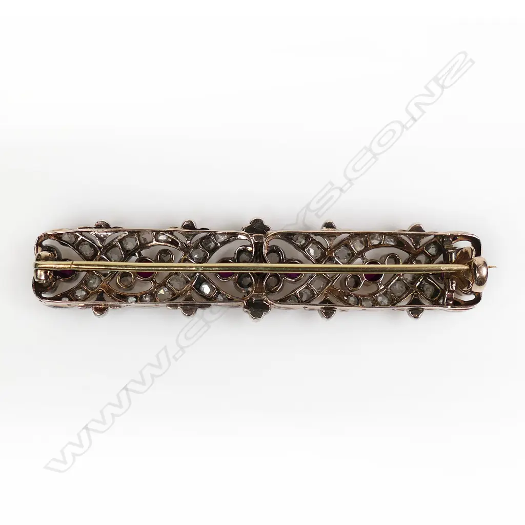 A late 19thC high carat gold, diamond and ruby brooch long rectangular form open work scrolls and floral designs festooned with graduating diamonds and highlighted with seven old facet cut rubies. Testing as 20ct. L.550mm. Image 1++