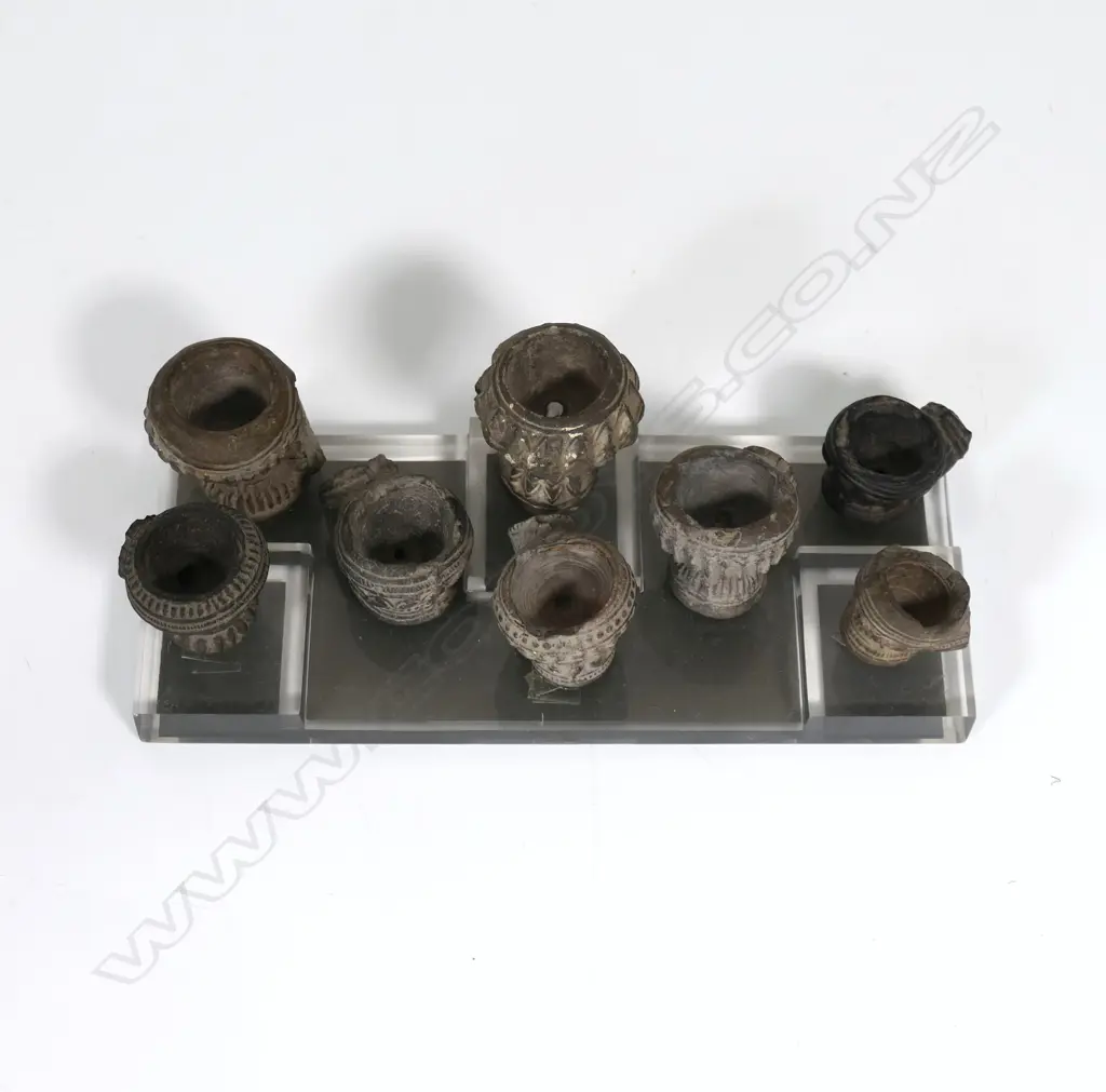 A collection of eight antique Burmese decorated and fired clay opium pipe bowls, the stems broken. Raised on clear Perspex stand. Image 1++