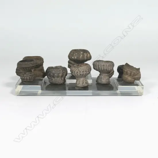 A collection of eight antique Burmese decorated and fired clay opium pipe bowls, the stems broken. Raised on clear Perspex stand.