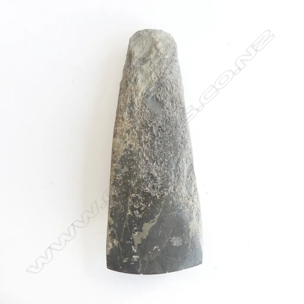 A Māori pre-European stone toki of large wide tapered form and grey tone, flaked at pole, fine all over pecking, the smooth polished curved blade with sharp edge. L.200mm Registered Y21216. Note: Buyer must be registered to purchase. Image 1++