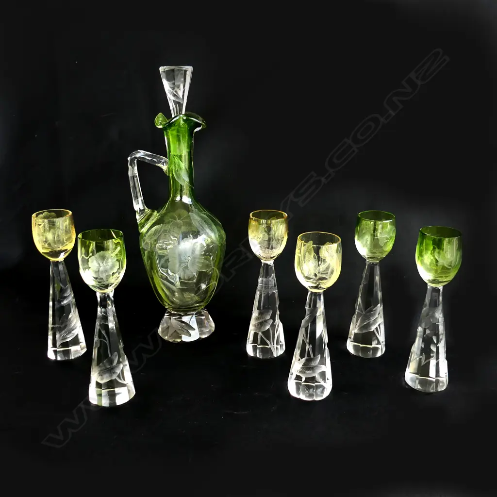 A  Moser decanter & 5 glasses (1 w staple repair) c.1910. The decanter with green body and clear handle and faceted base. Intaglio cut with florals. H.300mm. The conforming glasses include three green and two amber toned. H.160mm. one repaired. Note: Moser is a world recognised luxury glass manufacturer based in Karlovy Vary Image 1++
