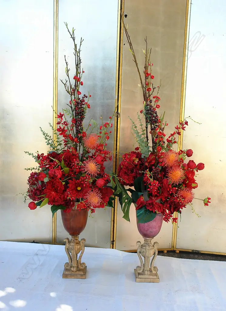 A pair of imitation floral displays in decorative gilded and wooden urns Image 1++